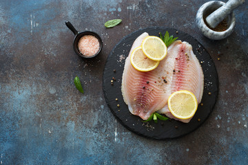Raw tilapia fillet with lemon and spices on a grunge stone background