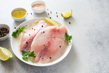 Raw tilapia fillet with lime and spices on a gray stone background close up