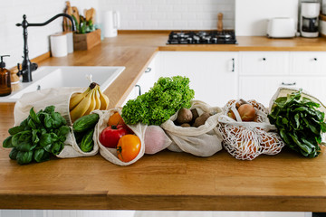 Fresh vegetables and fruits in eco cotton bags on table in the kitchen.