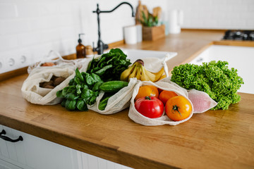 Fresh vegetables and fruits in eco cotton bags on table in the kitchen.