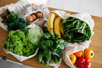 Fresh vegetables and fruits in eco cotton bags on table in the kitchen.