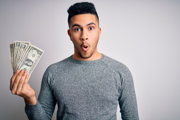 Young handsome man holding bunch of dollars banknotes over isolated white background scared in...