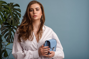 Fashionable woman wearing trendy white shirt, accessories, holding small blue faux leather bag....
