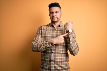 Young handsome man wearing casual shirt standing over isolated yellow background In hurry pointing...
