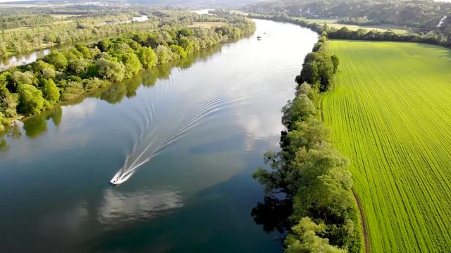 Scenic aerial view of the Seine river with boats and cargo barges and green fields in French countryside. Val d'Oise department, Ile-de-France, Northern France