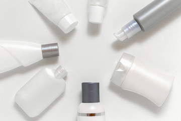 Cosmetic jars on a light background located around round copy space for text. Monochrome set of white and grey bottles