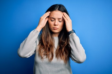 Young beautiful brunette woman wearing casual sweater standing over blue background suffering from...