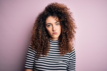 Young beautiful woman with curly hair and piercing wearing casual striped t-shirt depressed and...