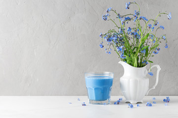Bouquet of blue flowers forget-me-not in vase with blue butterfly pea latte on concrete background. Still life