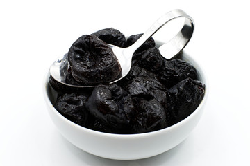 Dried prunes in a white bowl with a spoon isolated on white