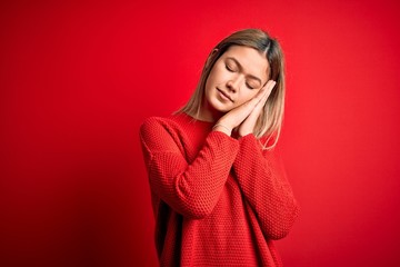 Young beautiful blonde woman wearing casual sweater over red isolated background sleeping tired dreaming and posing with hands together while smiling with closed eyes.