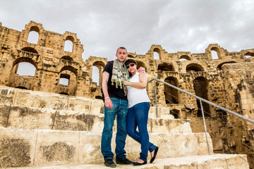 A couple of tourists in love pose against the backdrop of the Roman amphitheater in the city of El...