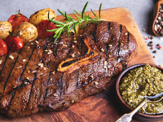 grilled beef steak with bone, roasted new potatoes  tomato with garlic on a wooden board, pesto sauce
