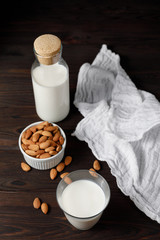 Fototapeta na wymiar Almond milk in a glass and a glass bottle on dark wooden background