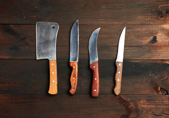 set of different kitchen knives with wooden handles on a brown background from boards