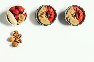 Healthy Vitamin Breakfast. Bananas, strawberries, nuts and dates in plates on a white background. Vegetarian and fitness food. Beautiful serving. Top view, copy space.