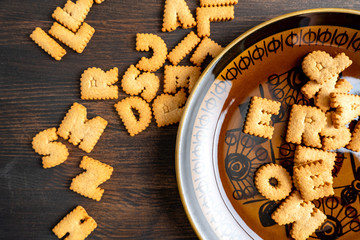 Letters of cracker biscuits scattered in rustic bowl and on rustic wooden backdrop.