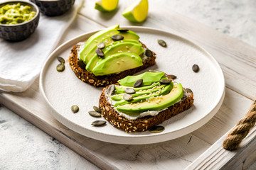 Avocado with cream cheese on grain bread on white tray and white concrete table