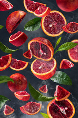 Blood oranges soar in the air along with citrus leaves.