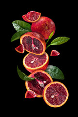 Blood oranges soaring in the air along with citrus leaves.