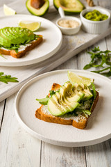 Toast with avocado, cream cheese,guacamole and arugula on white wooden table