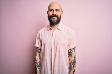 Obraz premium Handsome bald man with beard and tattoo wearing casual shirt over isolated pink background with a happy and cool smile on face. Lucky person.