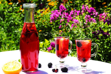 Still life with homemade fruit lemonade in a bottle and glasses on a table on background of flowers on outdoor