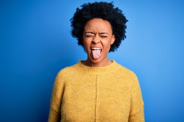 Fototapeta na wymiar Young beautiful African American afro woman with curly hair wearing yellow casual sweater sticking tongue out happy with funny expression. Emotion concept.
