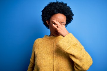 Fototapeta na wymiar Young beautiful African American afro woman with curly hair wearing yellow casual sweater smelling something stinky and disgusting, intolerable smell, holding breath with fingers on nose. Bad smell
