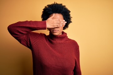 Fototapeta na wymiar Young beautiful African American afro woman with curly hair wearing casual turtleneck sweater covering eyes with hand, looking serious and sad. Sightless, hiding and rejection concept