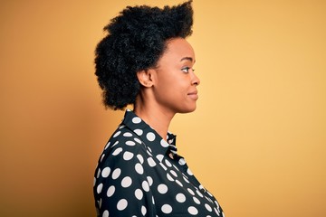 Obraz na płótnie Canvas Young beautiful African American afro woman with curly hair wearing casual shirt standing looking to side, relax profile pose with natural face with confident smile.