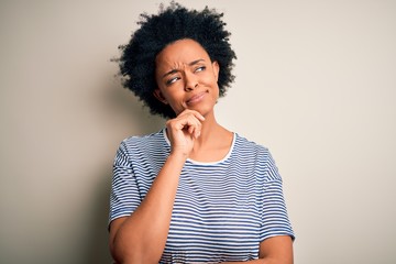 Fototapeta na wymiar Young beautiful African American afro woman with curly hair wearing striped t-shirt with hand on chin thinking about question, pensive expression. Smiling with thoughtful face. Doubt concept.