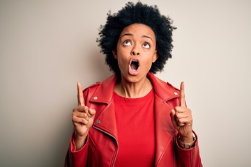 Young beautiful African American afro woman with curly hair wearing casual red jacket amazed and surprised looking up and pointing with fingers and raised arms.
