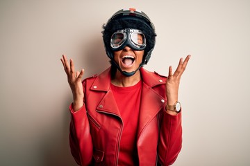 Young African American afro motorcyclist woman with curly hair wearing motorcycle helmet celebrating mad and crazy for success with arms raised and closed eyes screaming excited. Winner concept