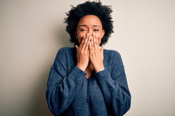 Young beautiful African American afro woman with curly hair wearing casual sweater laughing and embarrassed giggle covering mouth with hands, gossip and scandal concept - obrazy, fototapety, plakaty