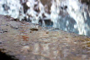 А drop falls on a wet stone, a waterfall in the background, a blurred background