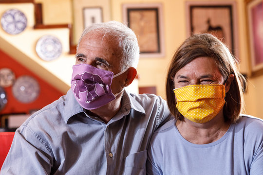 coppia di anziano con mascherine facciali colorate e divertenti si divertono seduti nel divano di casa loro