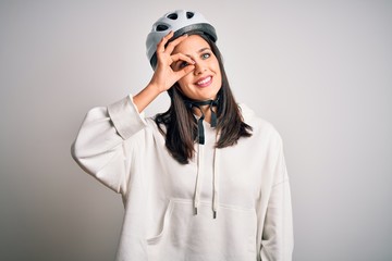 Young cyclist woman with blue eyes wearing bike helmet over isolated white background doing ok gesture with hand smiling, eye looking through fingers with happy face.