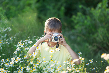 Child with professional camera is shooting flowers in sunny summer day on nature.