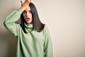 Young brunette woman with blue eyes wearing turtleneck sweater over white background surprised with...
