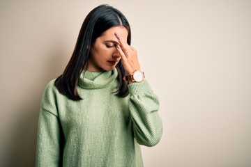 Young brunette woman with blue eyes wearing turtleneck sweater over white background tired rubbing nose and eyes feeling fatigue and headache. Stress and frustration concept.