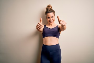 Fototapeta na wymiar Young beautiful blonde sportswoman doing sport wearing sportswear over white background approving doing positive gesture with hand, thumbs up smiling and happy for success. Winner gesture.