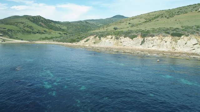 AERIAL DRONE APPROACH WITH TRANSPARENT BLUE SEA AND GREEN COAST IN NATURAL PARK IN ANDALUCIA