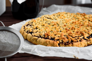 Grated pie on a sheet of parchment paper and a small sieve in the foreground. Pie on the side.
