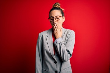 Young beautiful blonde businesswoman with blue eyes wearing glasses and jacket bored yawning tired covering mouth with hand. Restless and sleepiness.