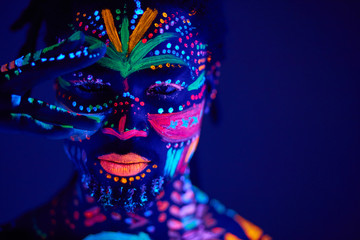 portrait of african man with ethnic pattern, neon makeup in ultraviolet light. fluorescent paints, luminescence prints. body art design of male posing in UV