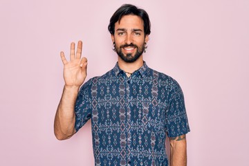 Young handsome hispanic bohemian man wearing hippie style over pink background showing and pointing up with fingers number three while smiling confident and happy.