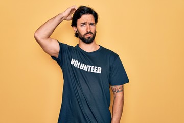 Young handsome hispanic volunteer man wearing volunteering t-shirt as social care confuse and wondering about question. Uncertain with doubt, thinking with hand on head. Pensive concept.
