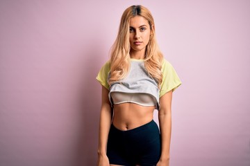 Fototapeta premium Young beautiful blonde sporty woman doing sport wearing sportswear over pink background with serious expression on face. Simple and natural looking at the camera.