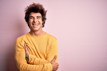 Fototapeta na wymiar Young handsome man wearing yellow casual t-shirt standing over isolated pink background happy face smiling with crossed arms looking at the camera. Positive person.